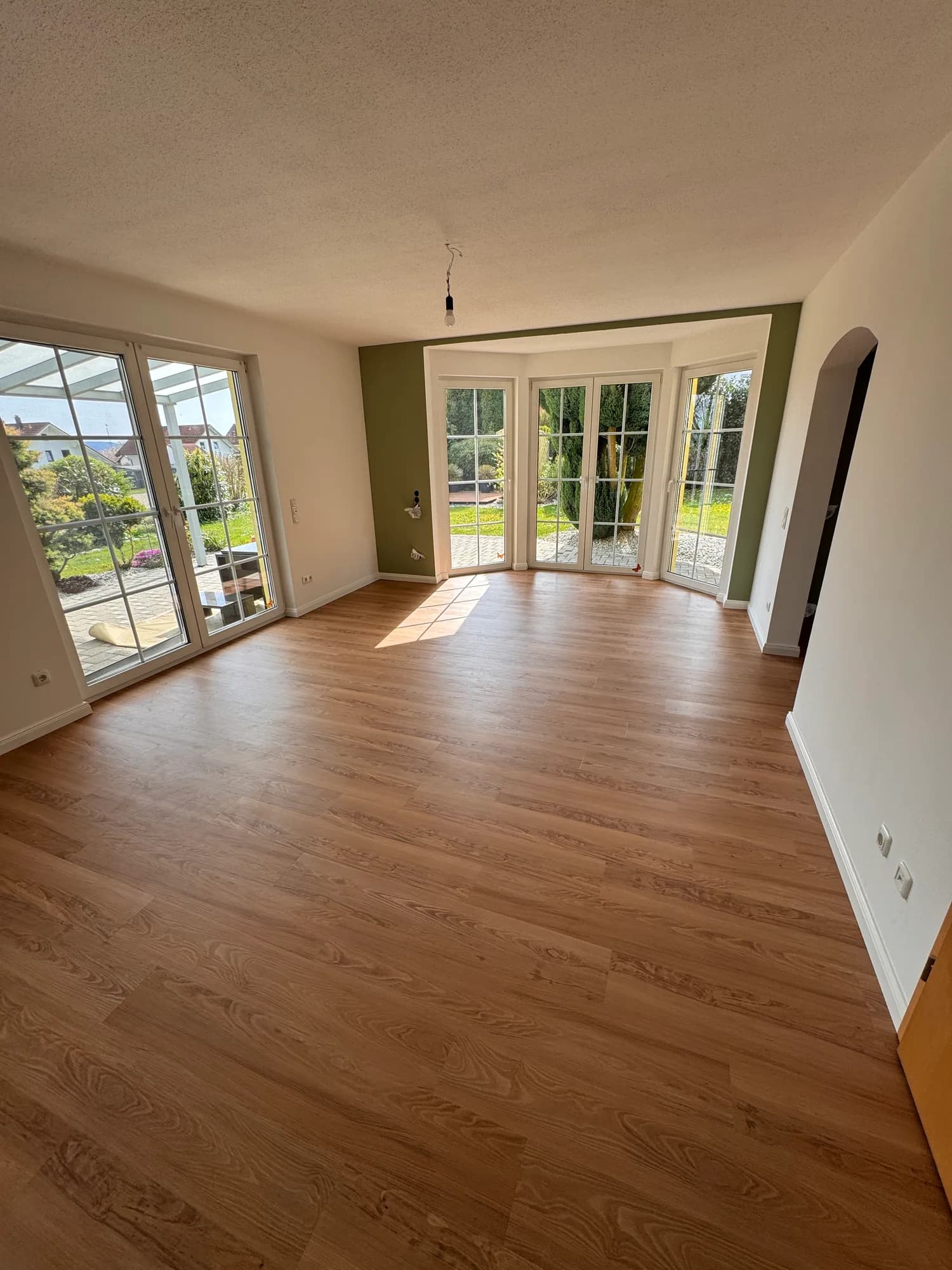 Sanierter, sonniger Wohnraum mit neuem Holzboden und Blick in den Garten