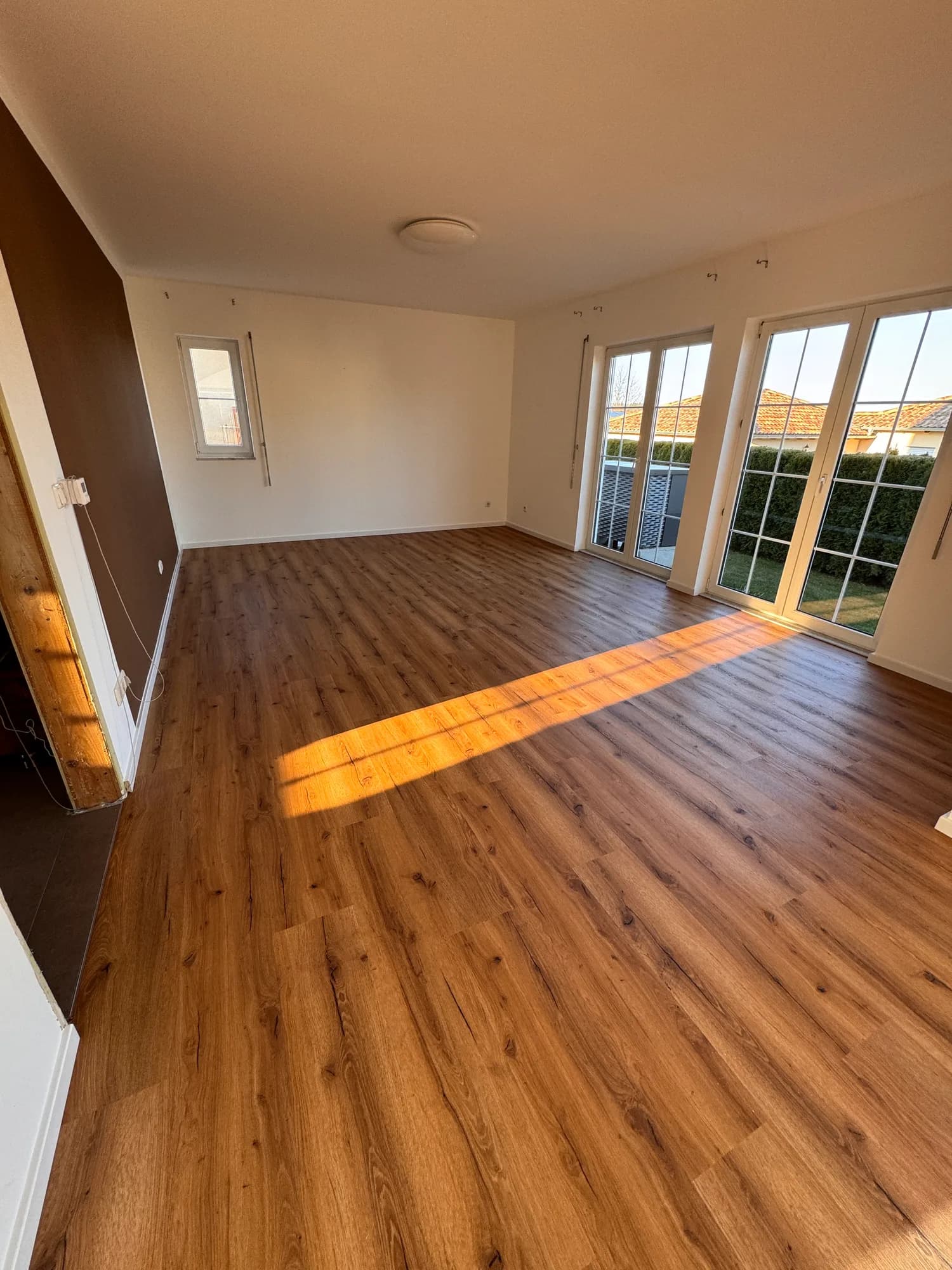 Wohnraum mit frisch verlegtem Boden in warmer Holzoptik und Terrassentüren